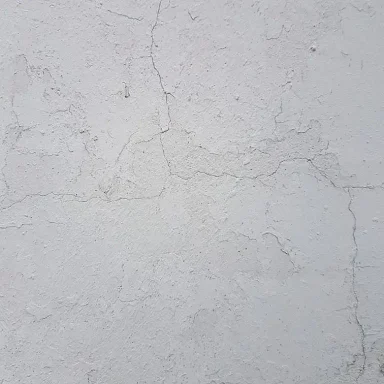 Graue Wand mit Rissen und unregelmäßiger Struktur.