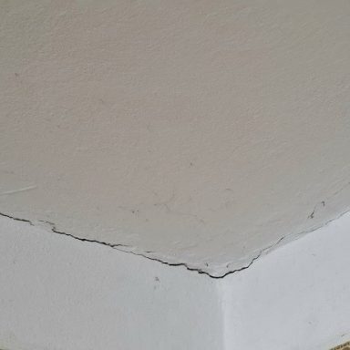 Ecke einer Wand mit unregelmäßiger Putzoberfläche und sichtbarem Riss.